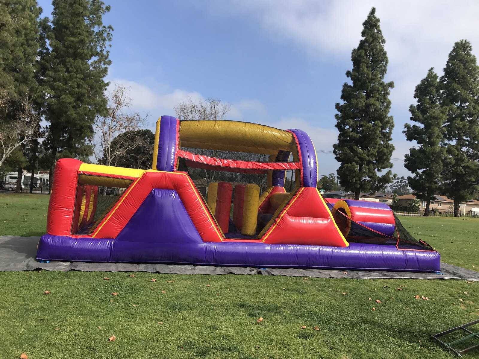 30ft backyard obstacle course rental in San Diego, full side profile on a park lawn showing pop-up obstacles and the exit slide