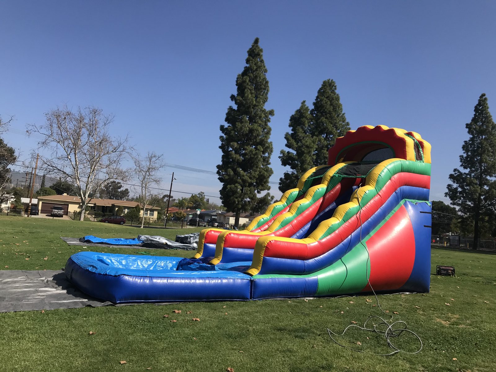 Water slide rental in San Diego, 18ft multi color setup wide view on grass with the tarp and splash pool in front