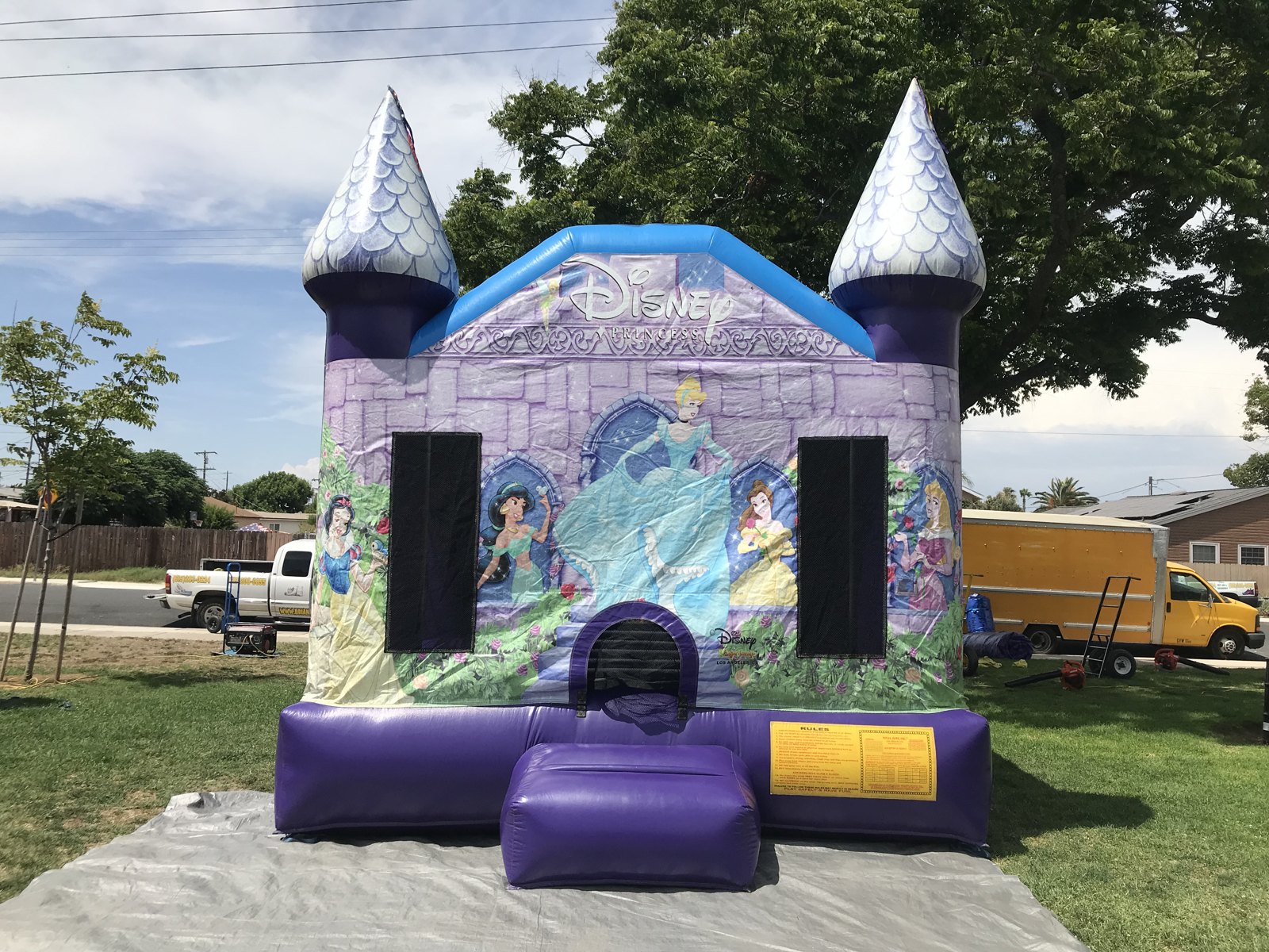 13x13 Disney Princess bounce house rental in San Diego — wide front view on a park lawn showing the entry ramp and safety rules panel