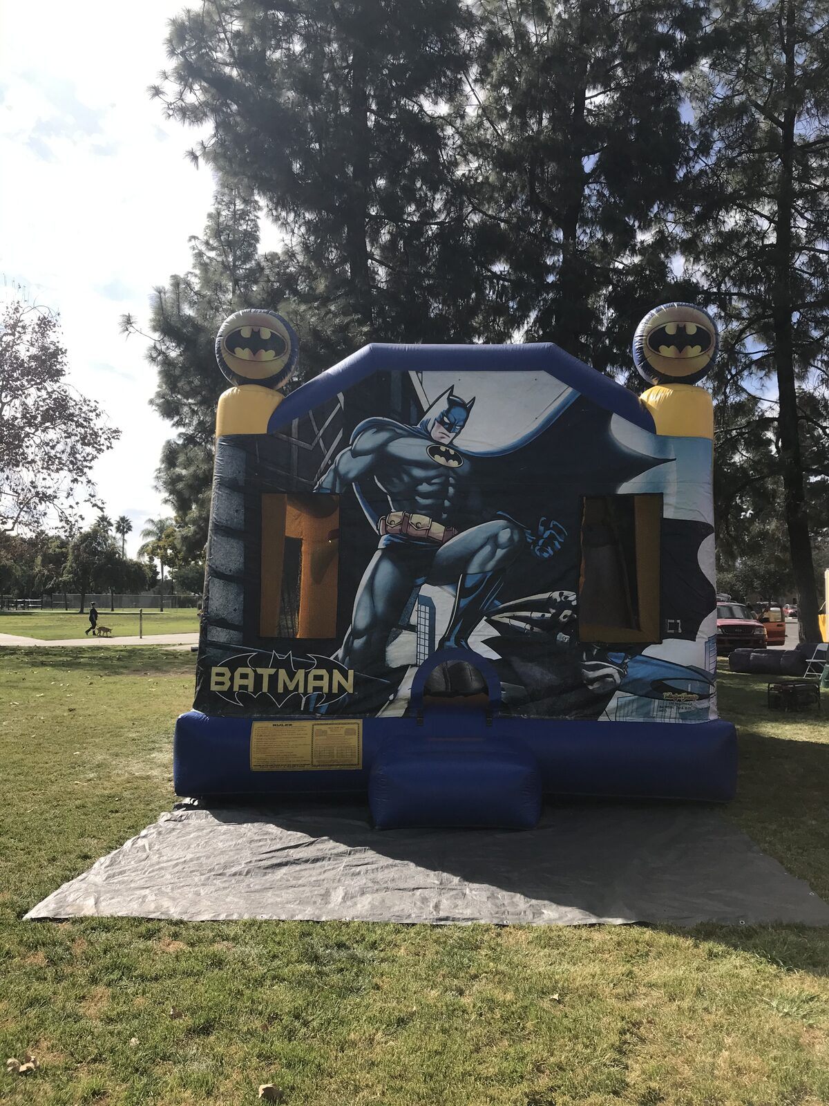 4n1 Batman combo bounce house rental in San Diego, front view of the navy Batman art panel with bat-signal towers on a tarp over park grass