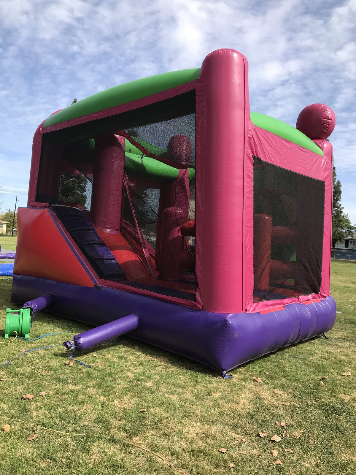 5n1 fairies combo bounce house rental in San Diego, rear corner view of the pink and green unit with mesh windows and red slide
