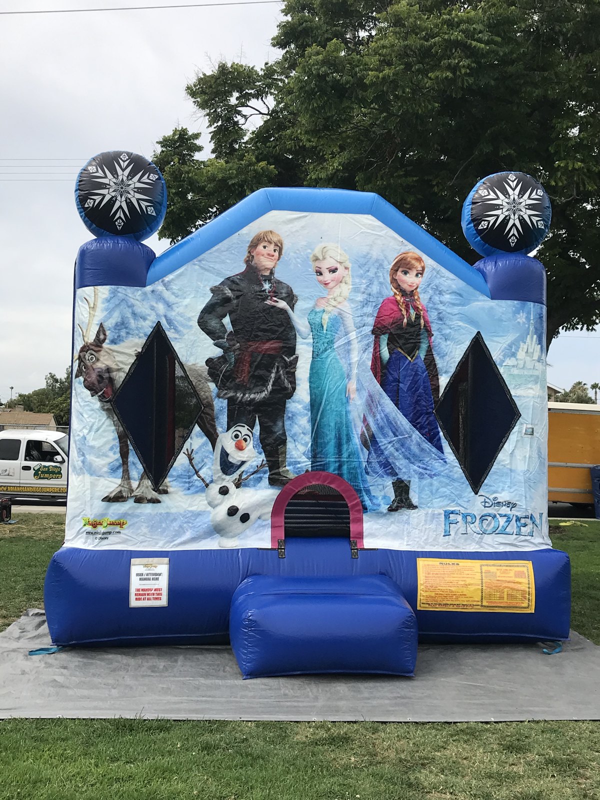 13x13 Frozen bounce house rental in San Diego — front view of the Disney Frozen castle with Elsa, Anna, Kristoff, Olaf, and Sven artwork and snowflake toppers on a park lawn