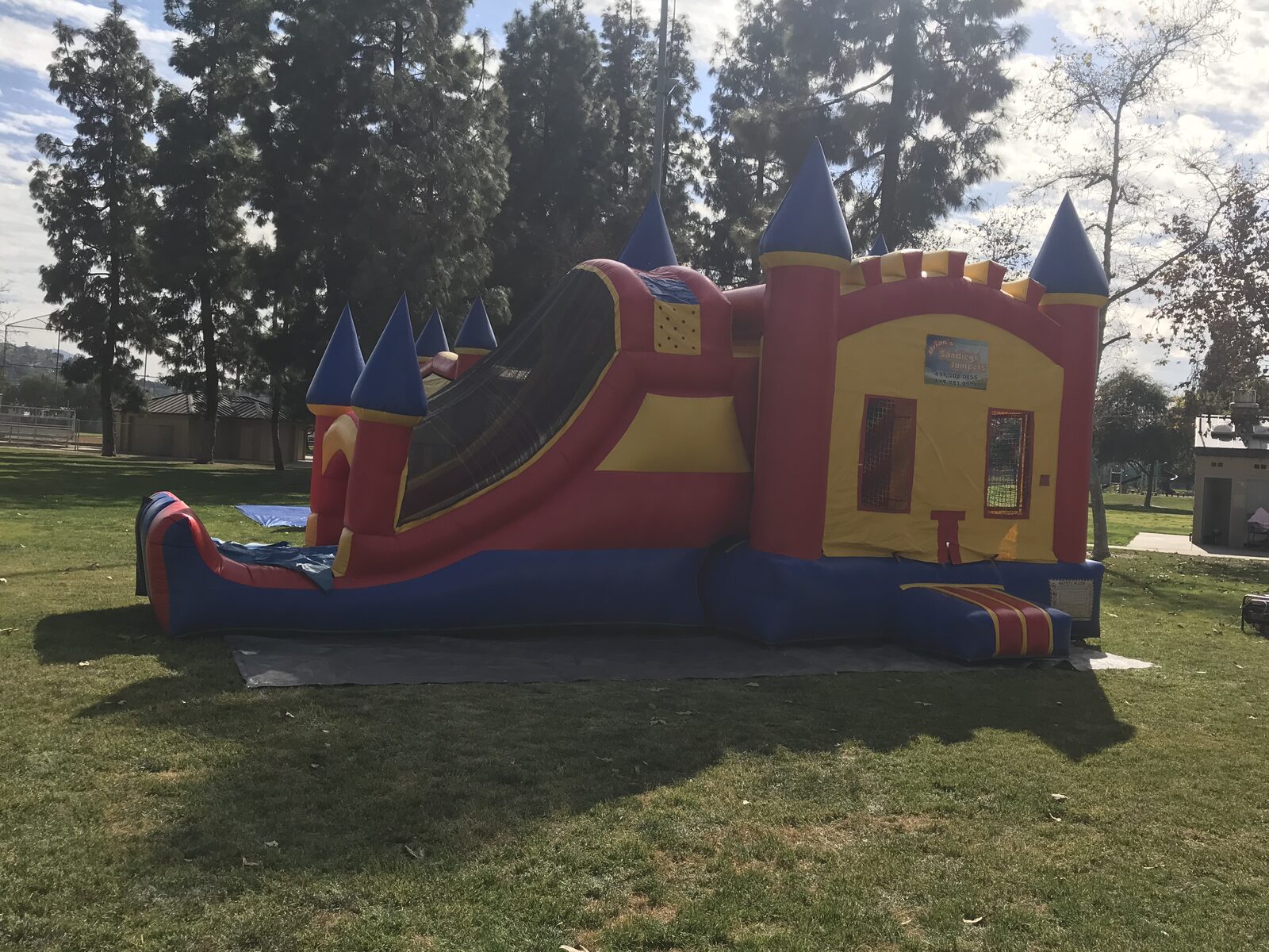 4n1 blue castle combo bounce house rental in San Diego, side view of the red, yellow, and blue castle with blue turrets and attached slide on park grass