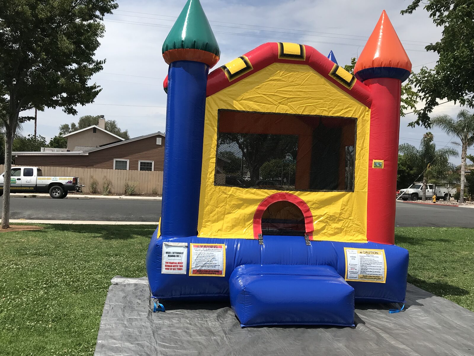 12x14 multi color castle mini bounce house rental in San Diego, straight-on front view of the arched entry and blue step in a front yard