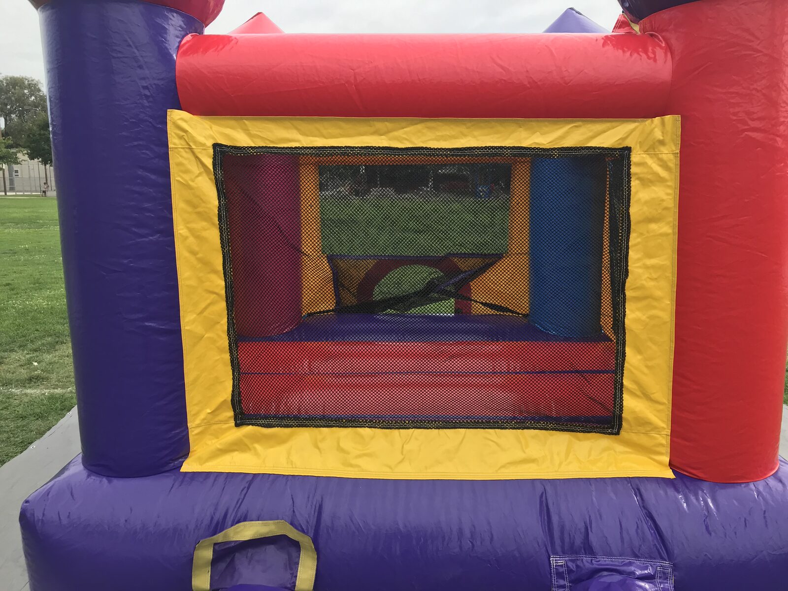 10x12 multi color castle mini bounce house rental in San Diego, close view of the yellow-framed mesh window and red, blue and purple castle walls