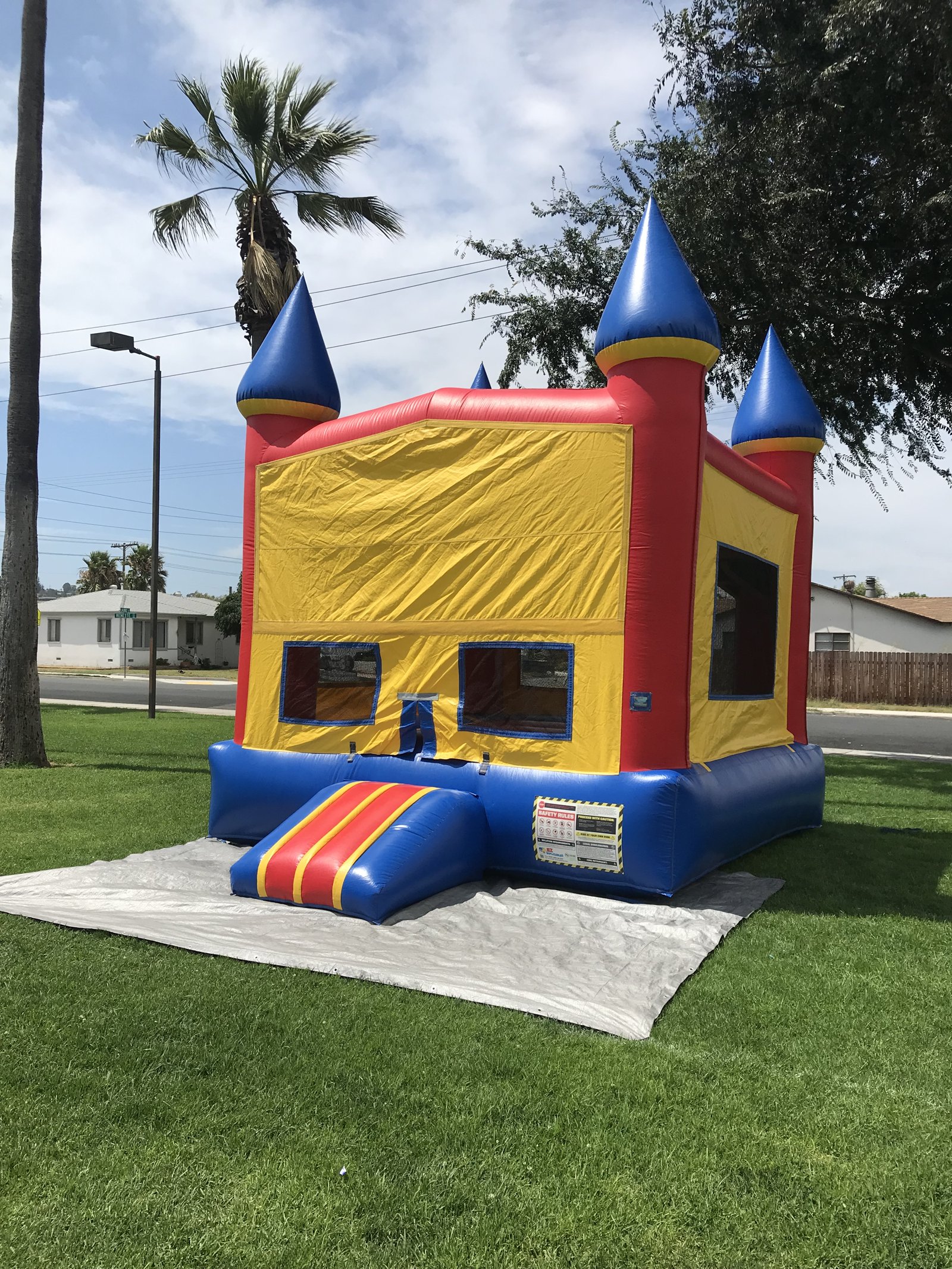 13x13 Blue Castle Banner bounce house rental in San Diego — angled front view on a protective tarp showing the entry ramp and mesh safety windows