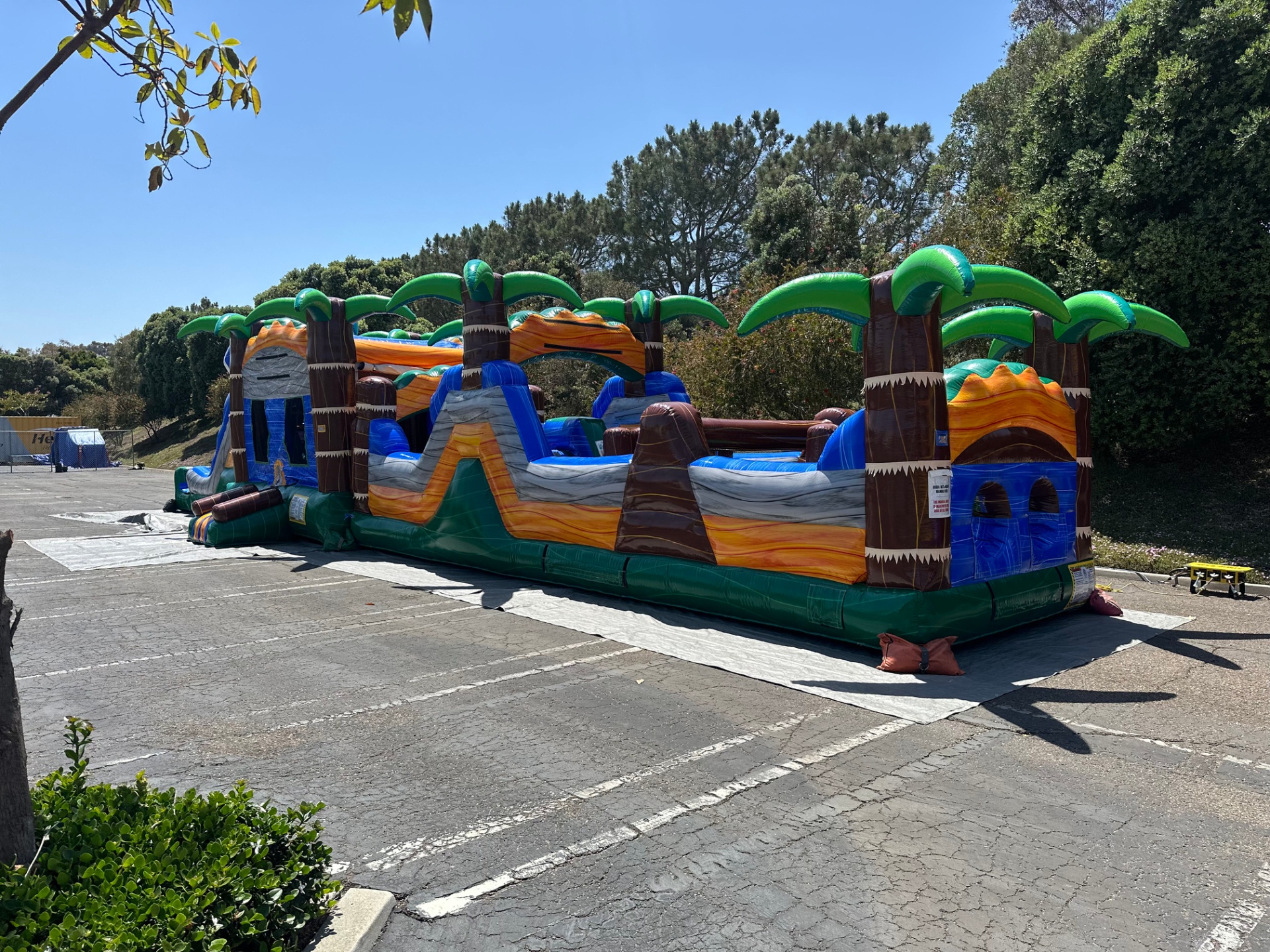 63ft tropical obstacle course rental in San Diego, full side view of the palm-tree course with blue marble obstacles set up on a lot