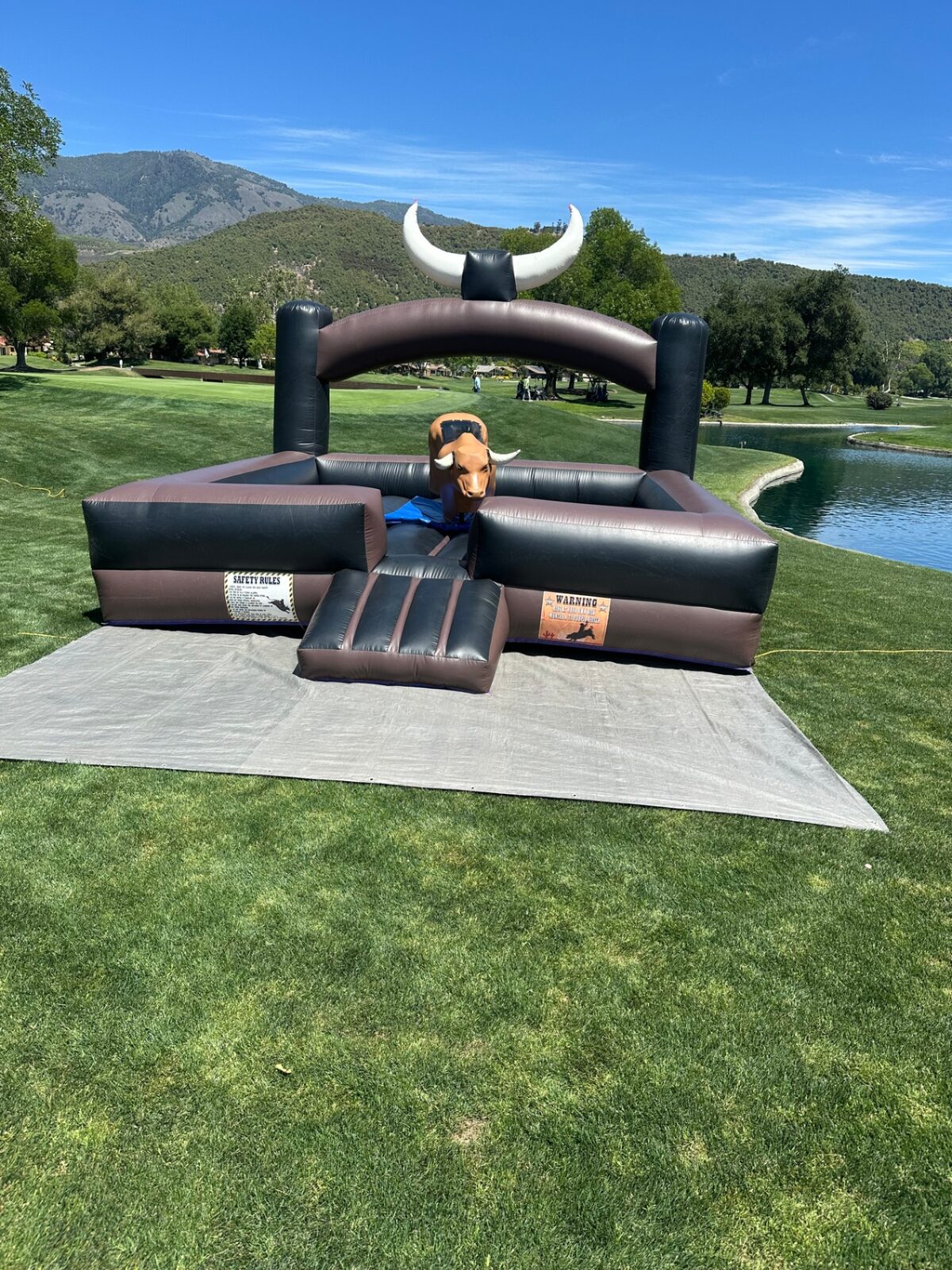 Mechanical bull rental in San Diego, 15x15 setup front view on grass showing the safety rules and warning banners