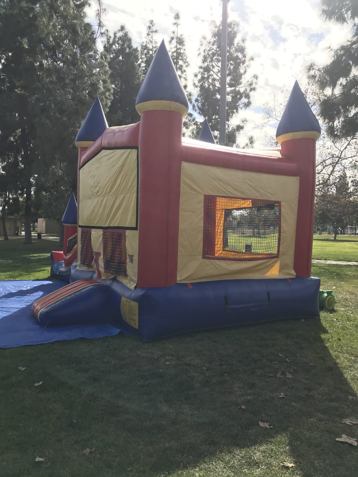 4n1 blue castle banner combo bounce house rental in San Diego, corner view of the red and yellow castle with blue turrets and banner panel at a park