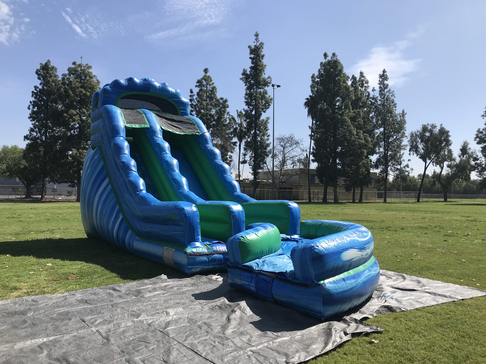 Dry slide rental in San Diego, 20ft green and blue setup angled view on grass with trees behind