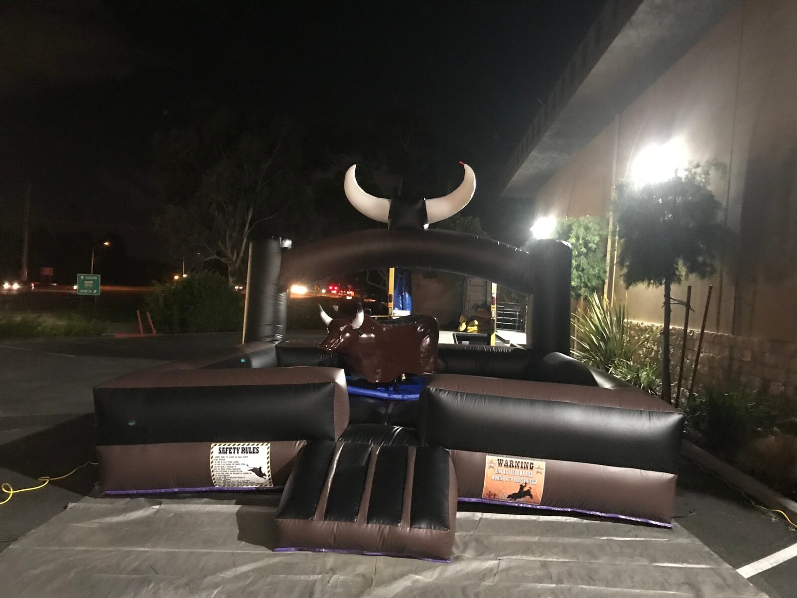 Mechanical bull rental in San Diego, 15x15 setup at night in a lit parking lot on a protective tarp