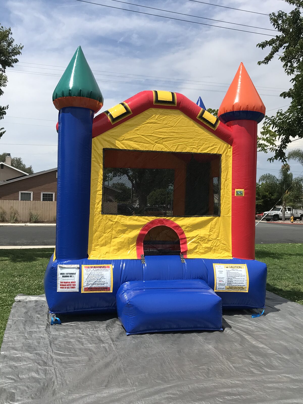 12x14 multi color castle mini bounce house rental in San Diego, front view of the yellow and blue castle with green and orange turrets on a tarp