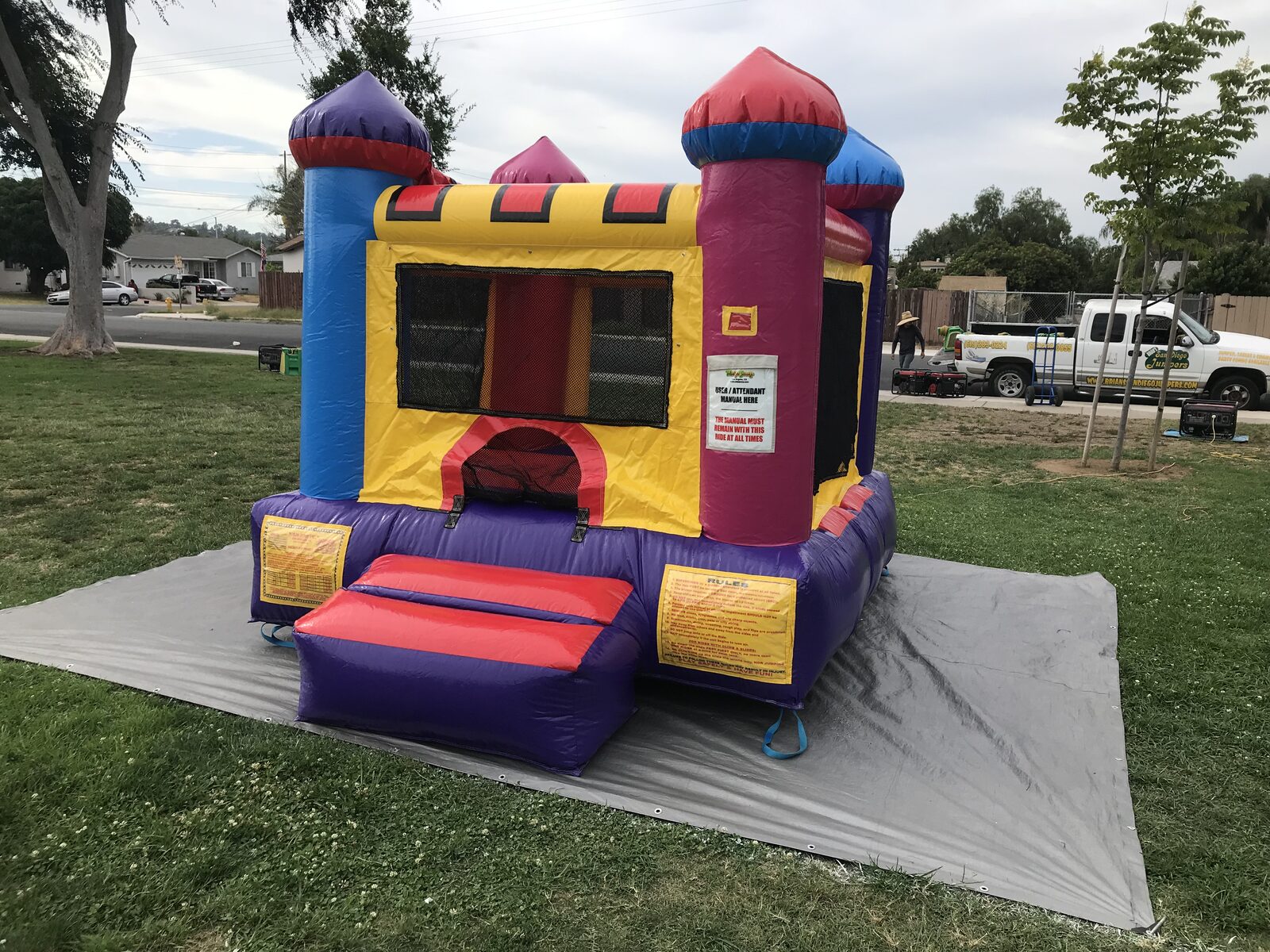 10x12 multi color castle mini bounce house rental in San Diego, three-quarter view with red and purple entry step on a tarp in a front yard
