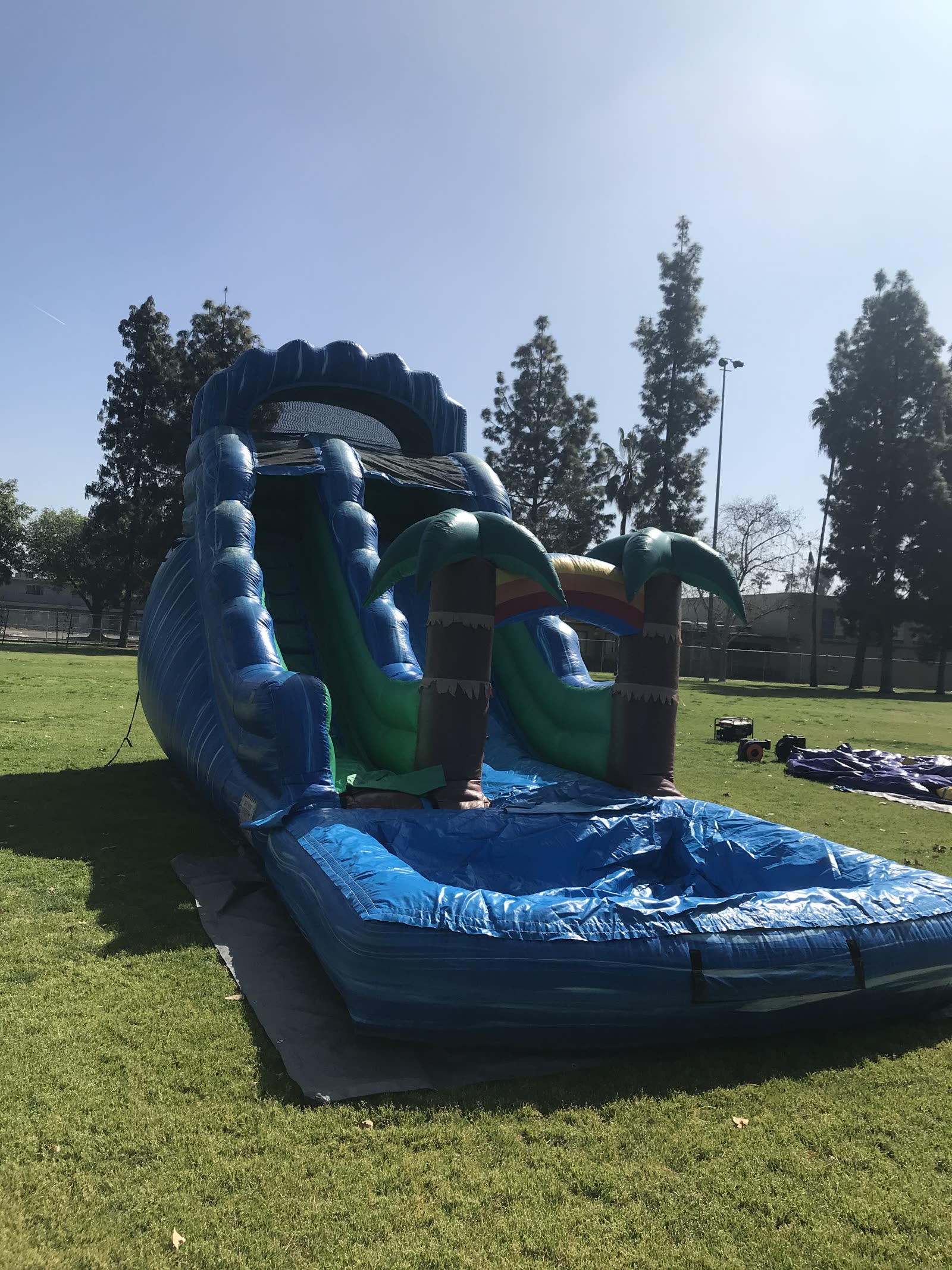Water slide rental in San Diego, 18ft palm tree setup on a school field with blue wave walls, inflatable palm trees and a splash pool