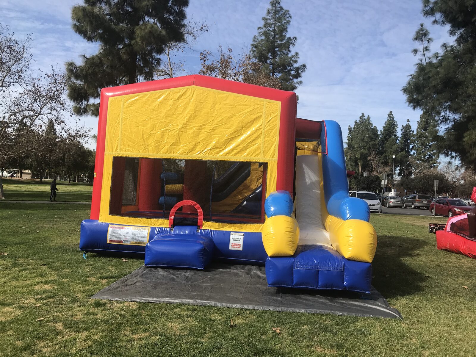 6n1 banner combo bounce house rental in San Diego, front view of the red, yellow, and blue banner unit with side slide set up on a tarp at a park
