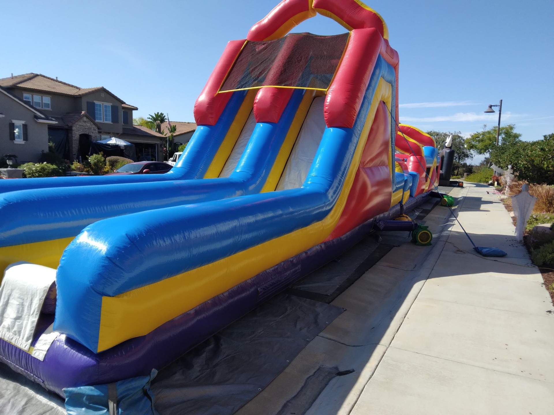 70ft monster obstacle course rental in San Diego, low view up the tall dual-lane slide set up along a residential driveway