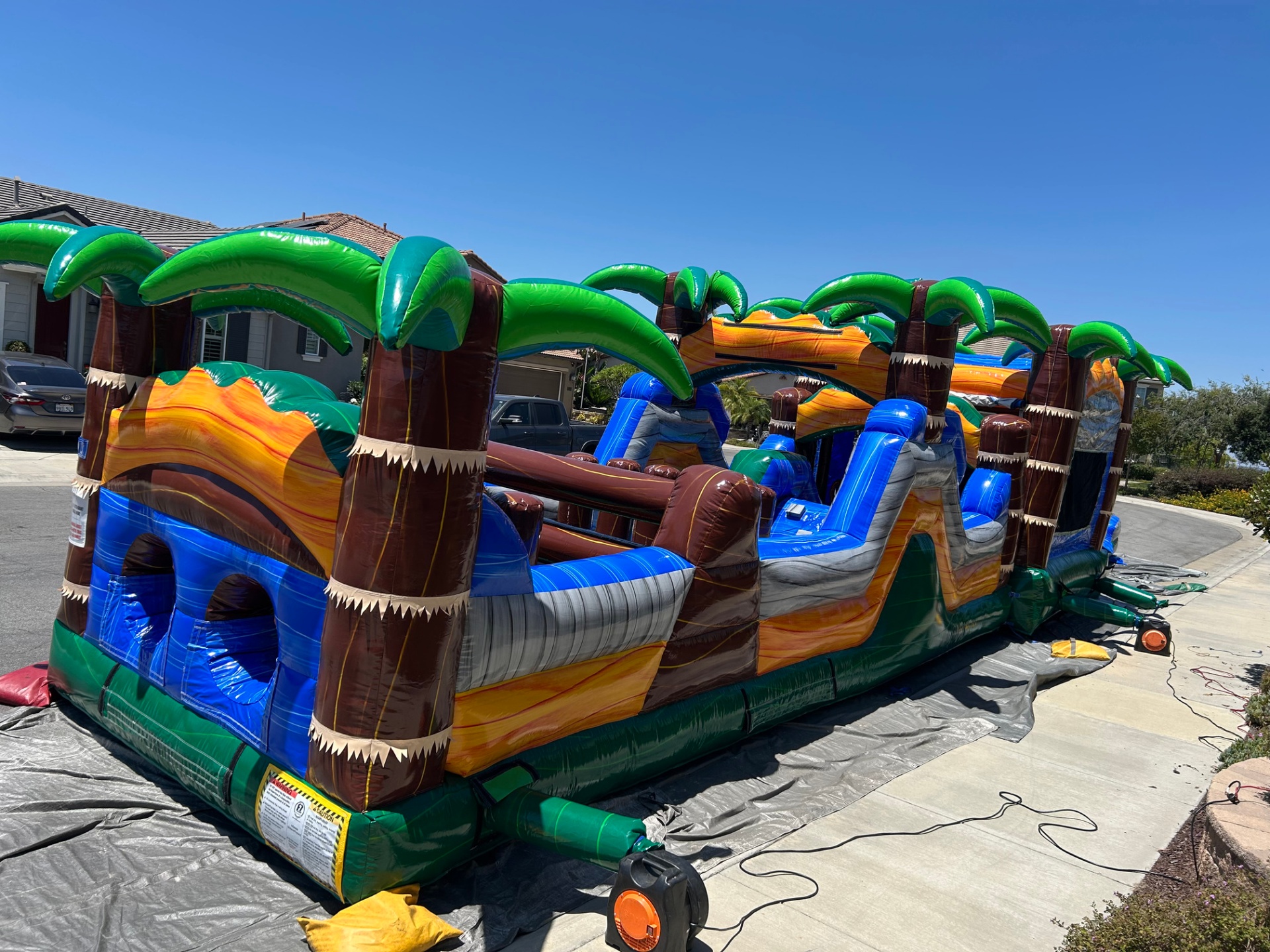 63ft tropical obstacle course rental in San Diego, angled view of the crawl tunnels and pop-up obstacles on a driveway