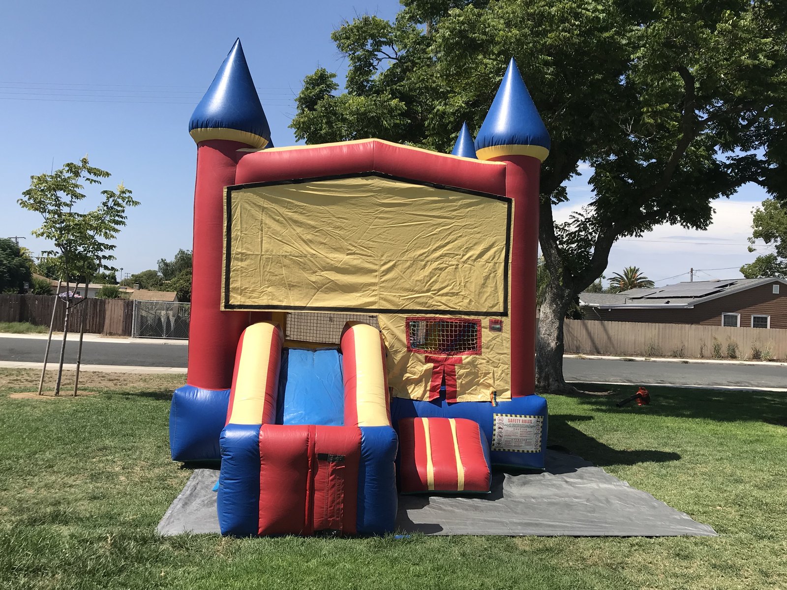 2n1 blue castle combo bounce house rental in San Diego, wide front view of the unit staked on a tarp at a neighborhood park
