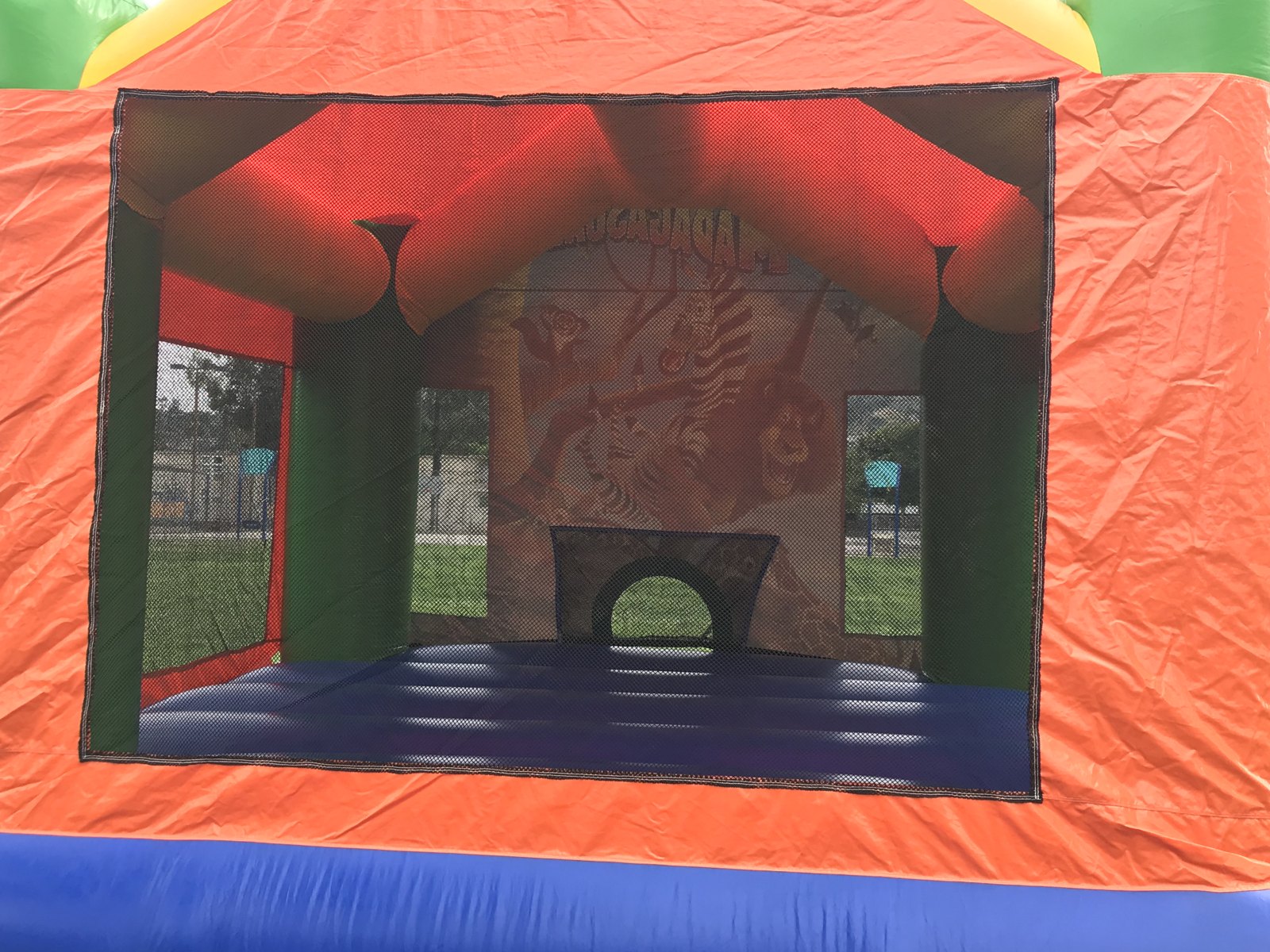 13x13 Madagascar bounce house rental in San Diego — inside view of the blue jumping floor and basketball hoop through the mesh window