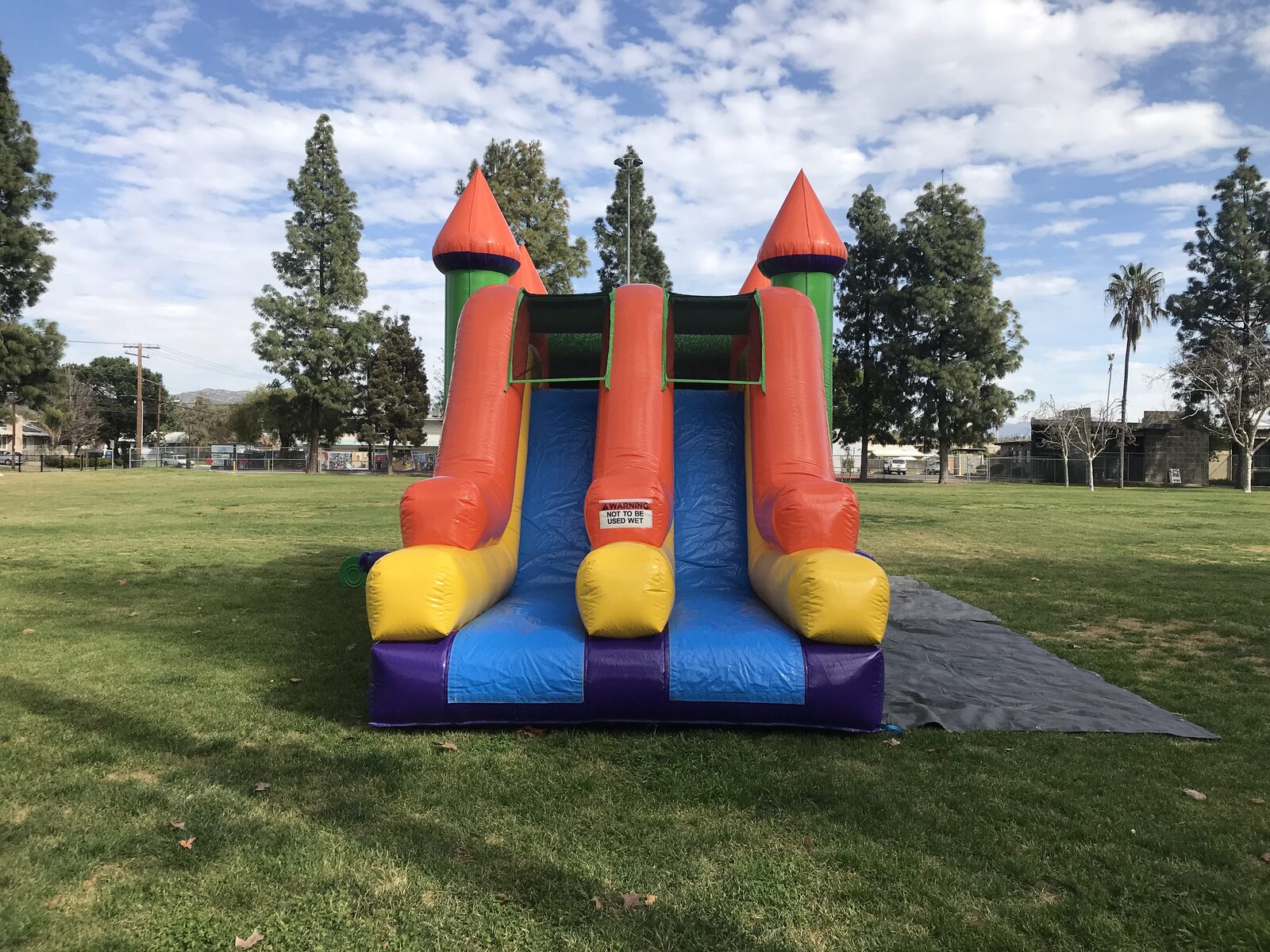 4n1 multi-color castle banner combo bounce house rental in San Diego, straight-on view of the two side-by-side orange slide lanes with green turrets and purple base on park grass