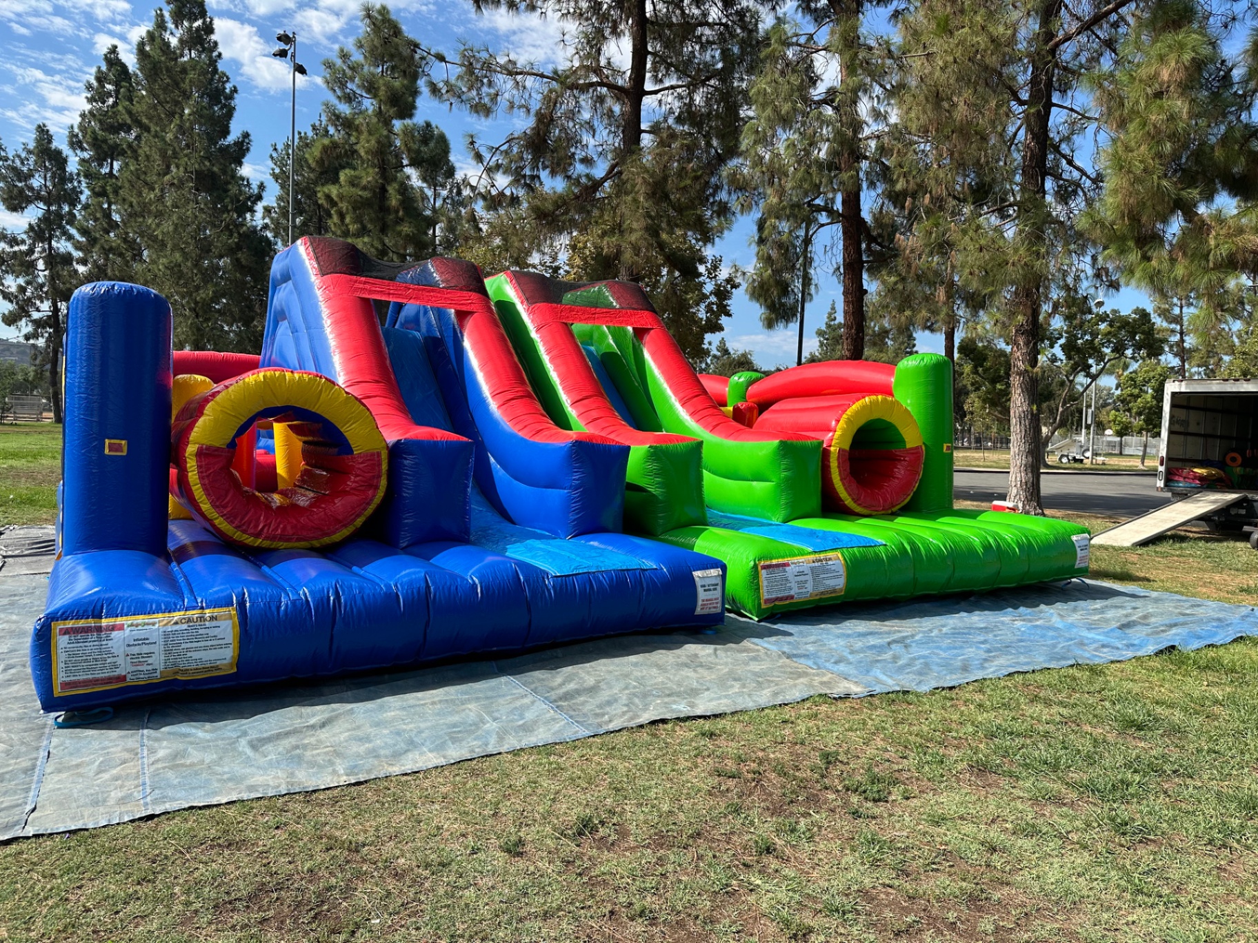 Dual lane challenge course obstacle rental in San Diego, blue and green lanes set up side by side on a park lawn with both slide exits facing forward