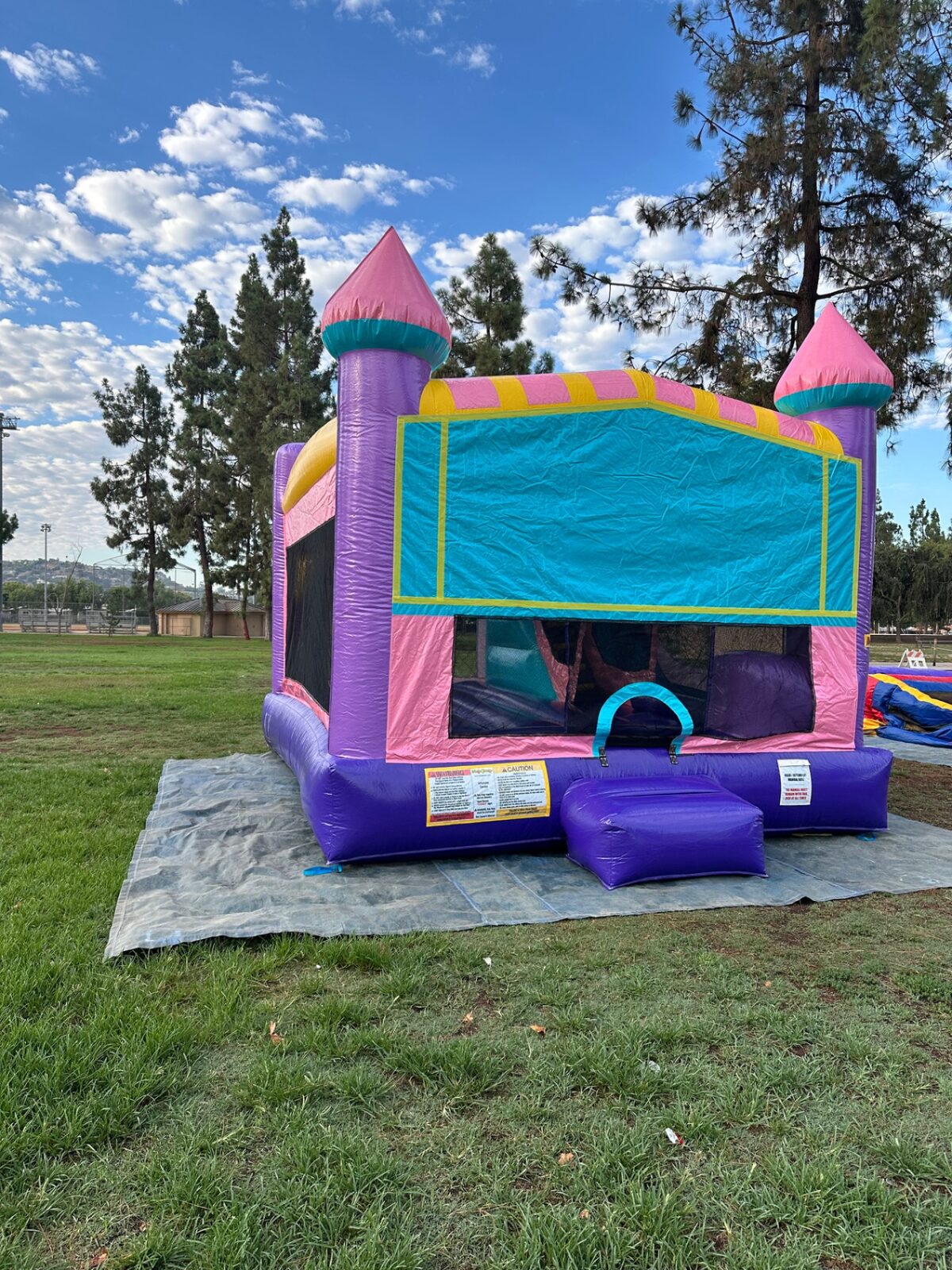 4n1 dazzling castle combo bounce house rental in San Diego, angled view of the front banner panel and purple base set up on a tarp over grass