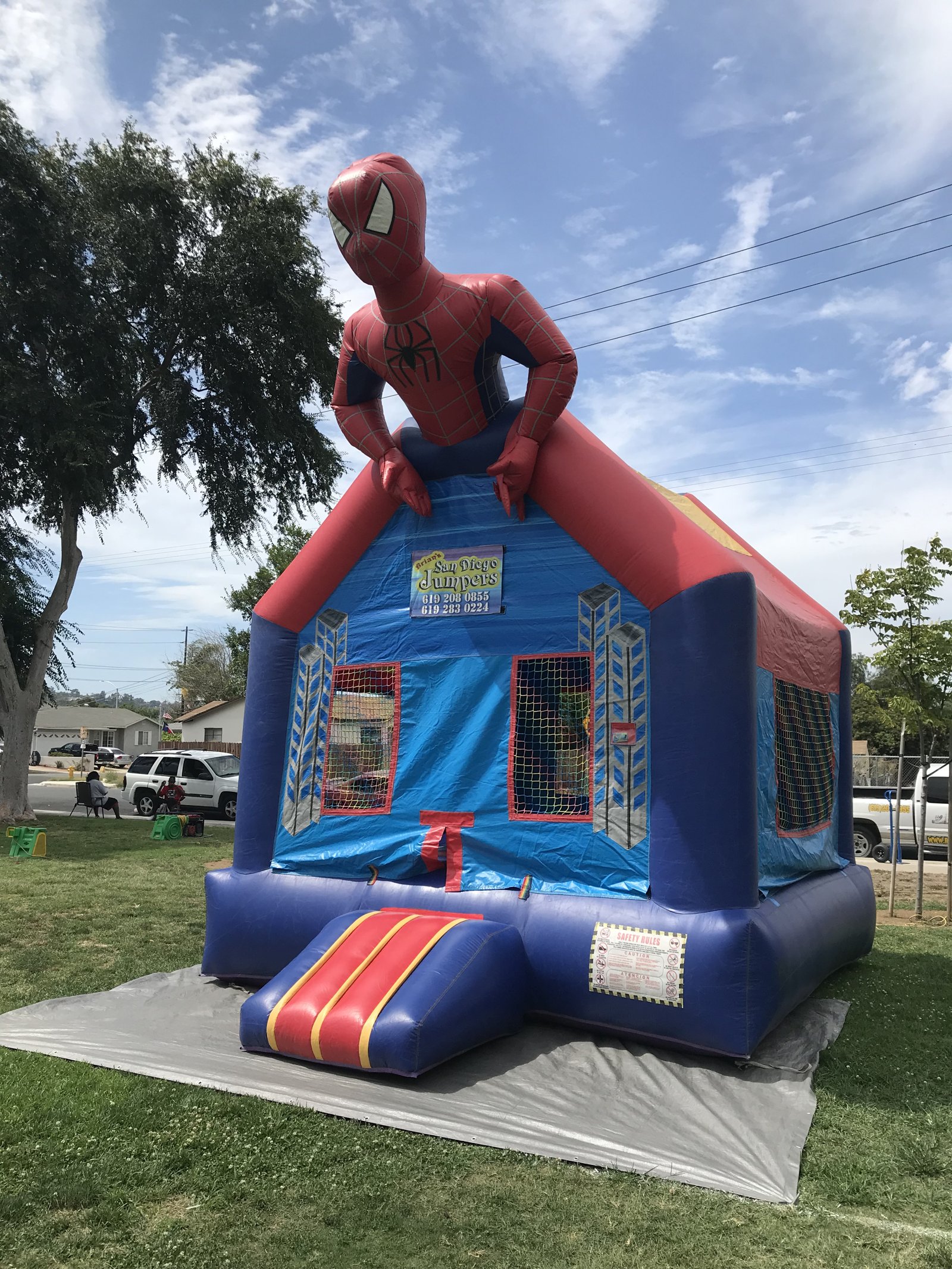 13x13 Spider-Man bounce house rental in San Diego — side-angled park setup showing the blue base and skyscraper artwork