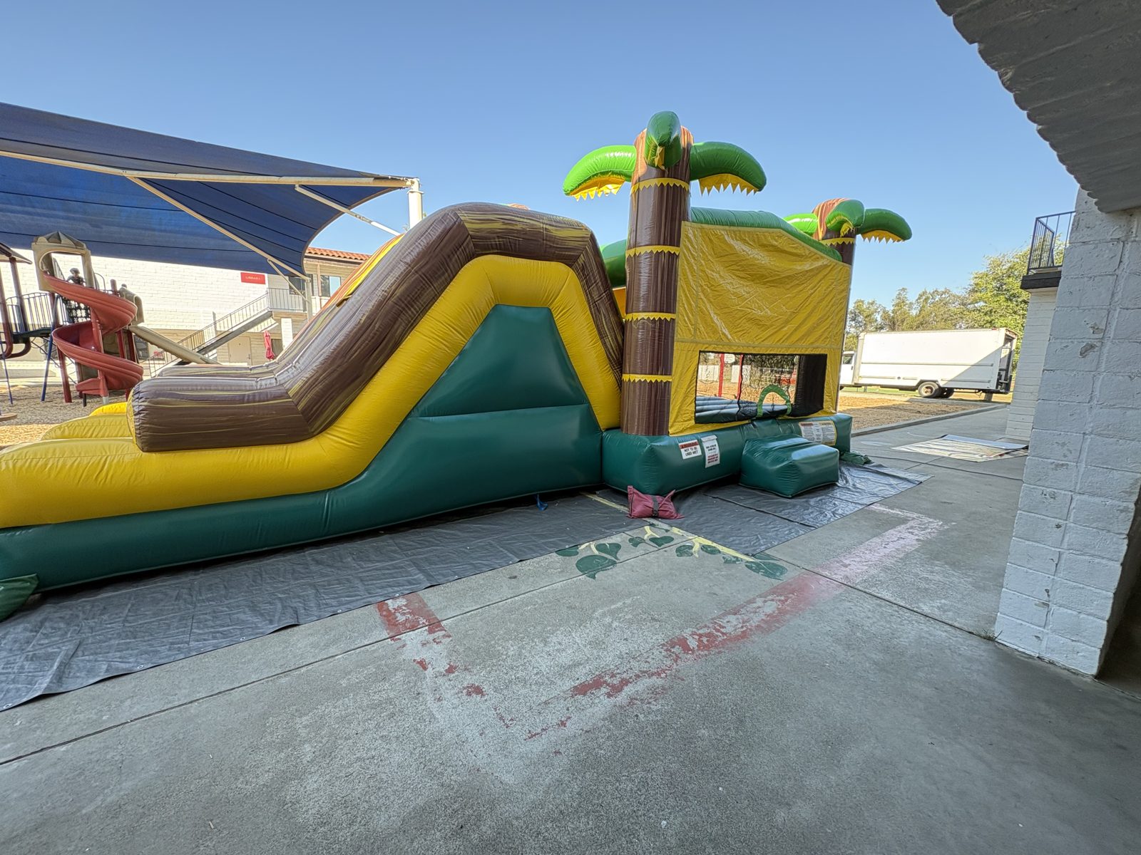 4n1 tropical oasis dual slide combo bounce house rental in San Diego, side view of the brown and yellow slide on a school blacktop