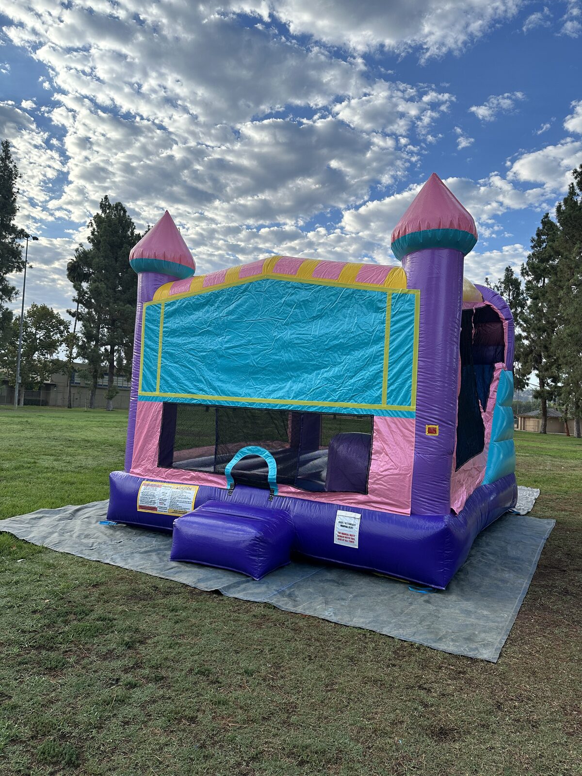 4n1 dazzling castle combo bounce house rental in San Diego, three-quarter front view showing the pink turrets and mesh-window jump area on a park field