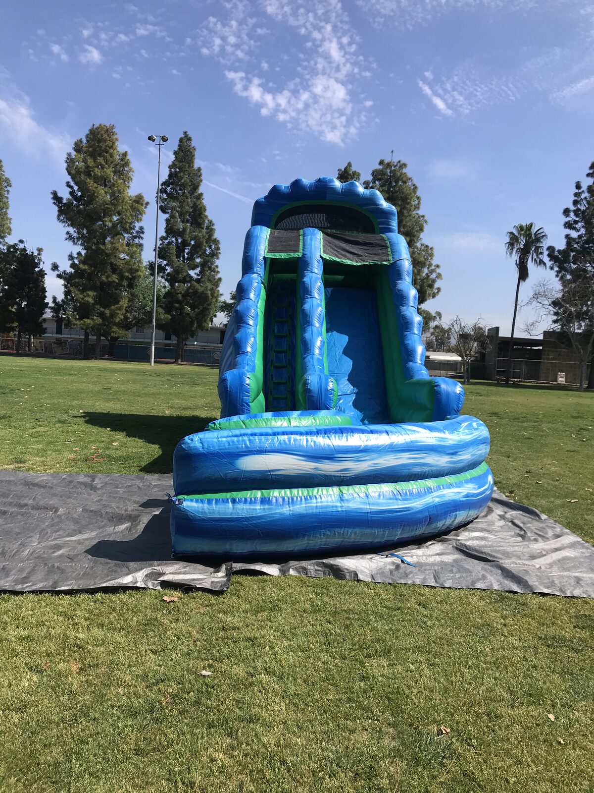 Dry slide rental in San Diego, 20ft green and blue setup front view showing the climbing wall and mesh top