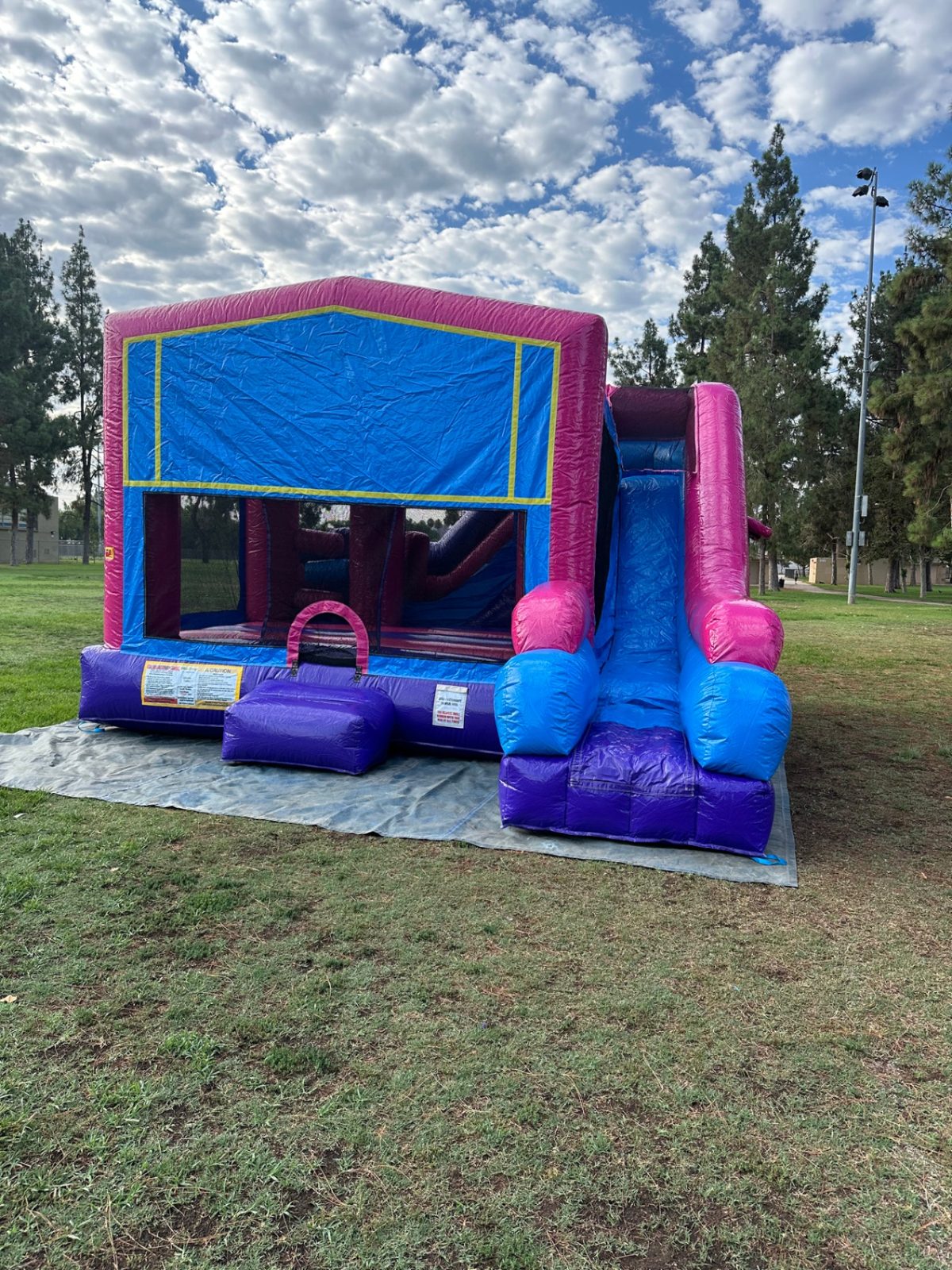 6n1 pink banner combo bounce house rental in San Diego, front view of the blue banner panel, pink frame and front slide at a park
