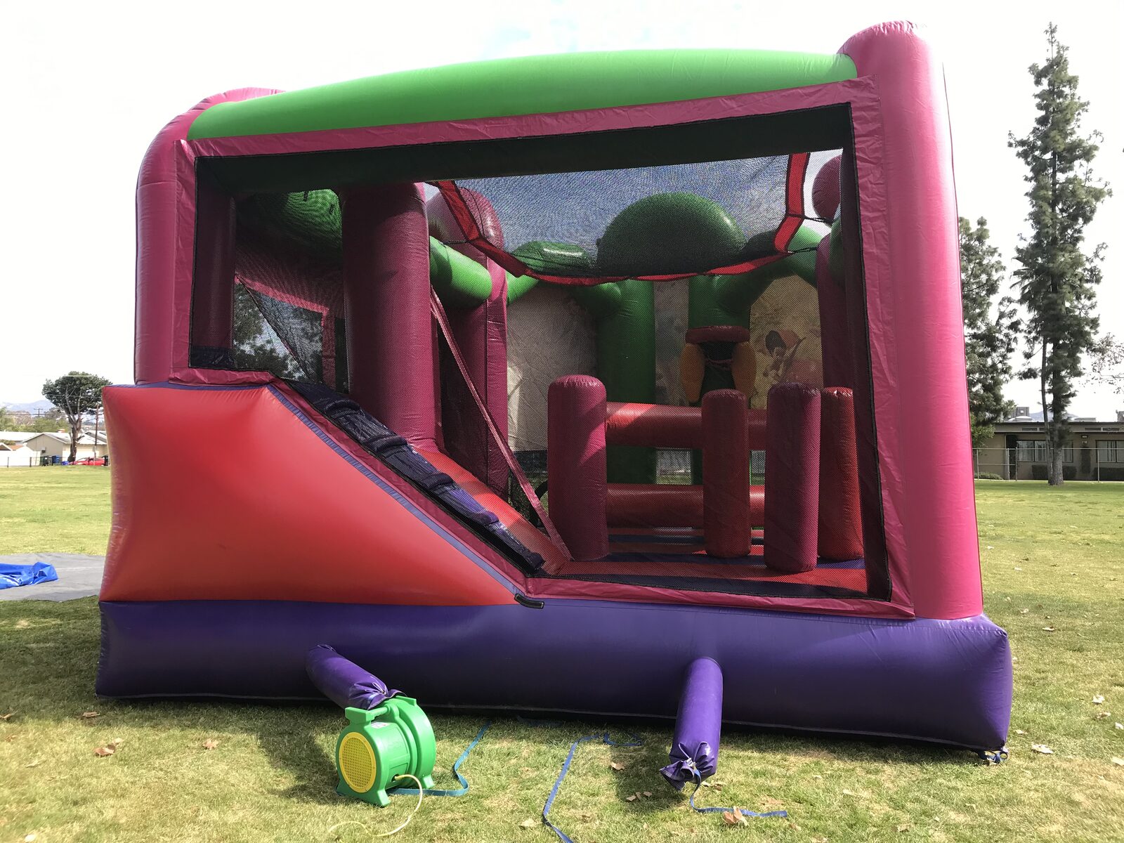 5n1 fairies combo bounce house rental in San Diego, back view showing the slide, climbing wall and pop-up obstacles inside with the blower hooked up