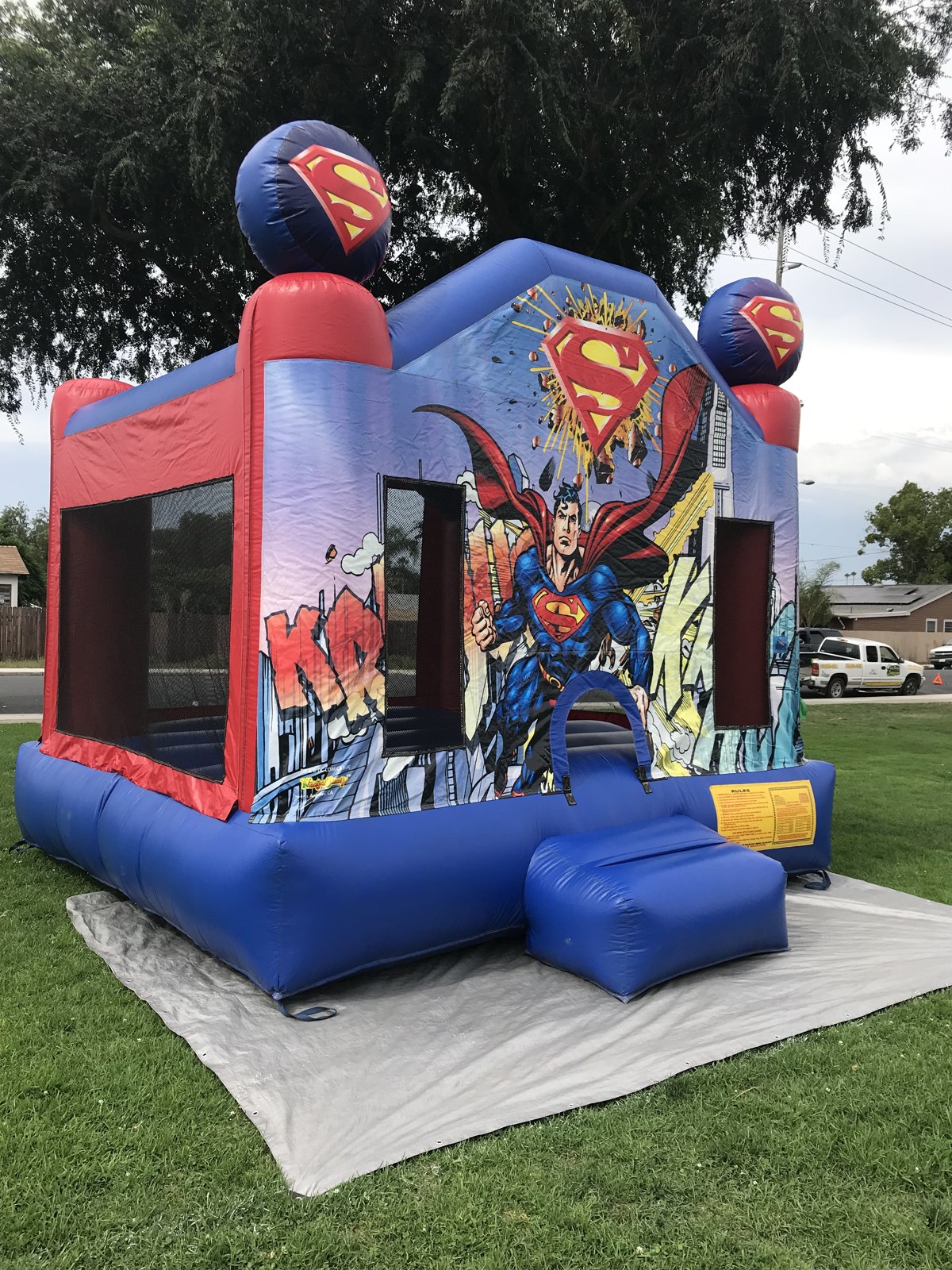 13x13 Superman bounce house rental in San Diego — side-angled view showing the red mesh safety windows and comic city artwork
