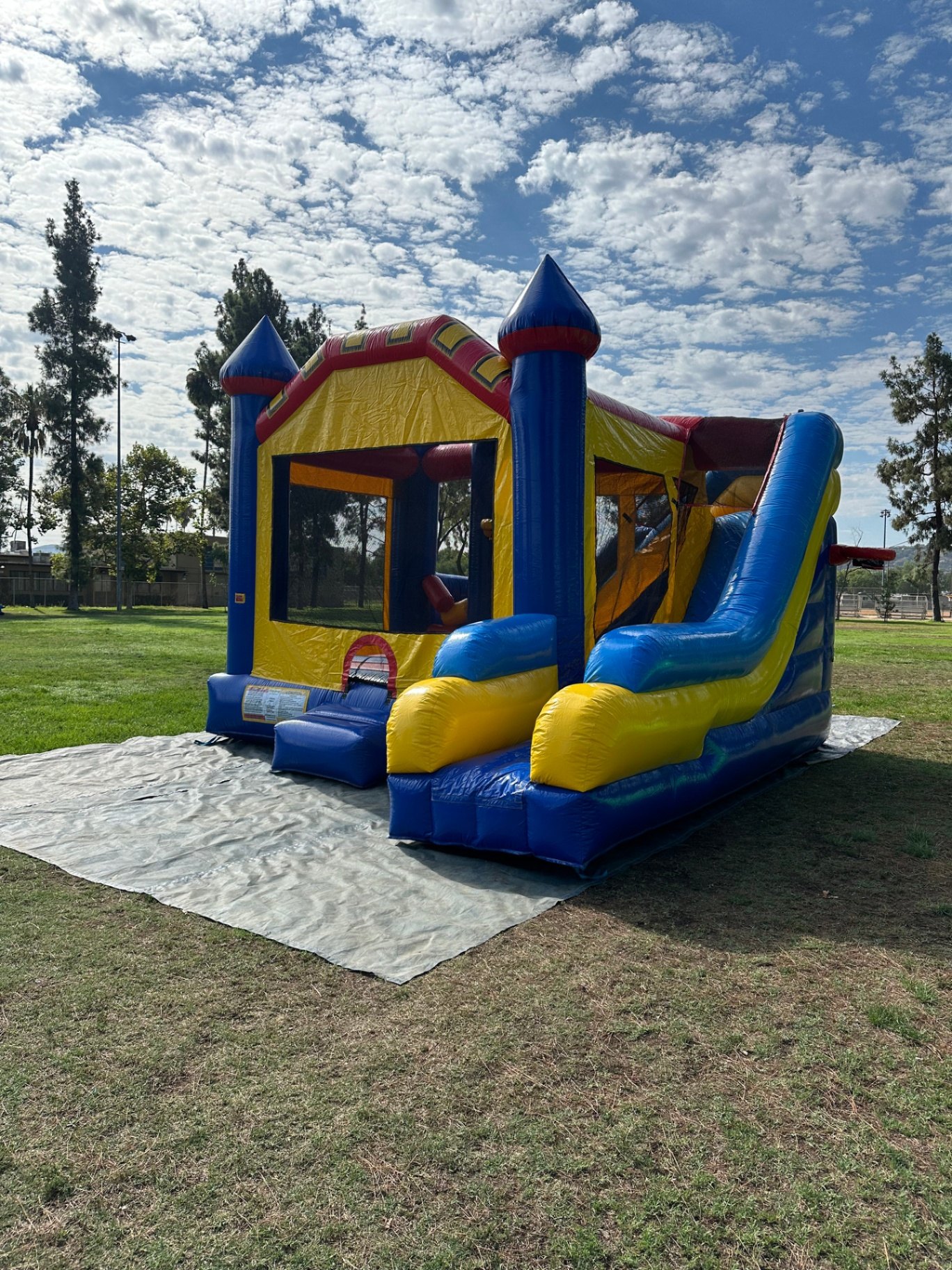 6n1 blue castle combo bounce house rental in San Diego, wide angled view of the whole unit on grass under a cloudy blue sky
