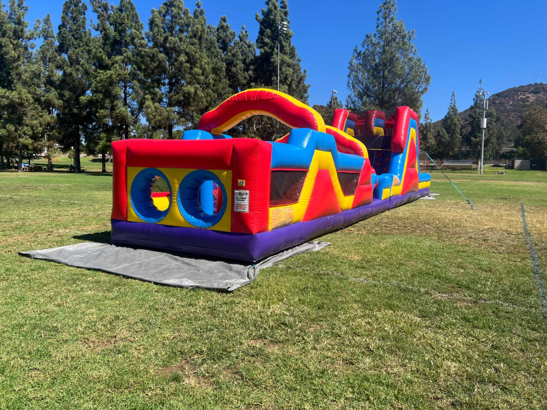 70ft monster obstacle course rental in San Diego, entry end with twin crawl-through tunnels and red arch on a park lawn