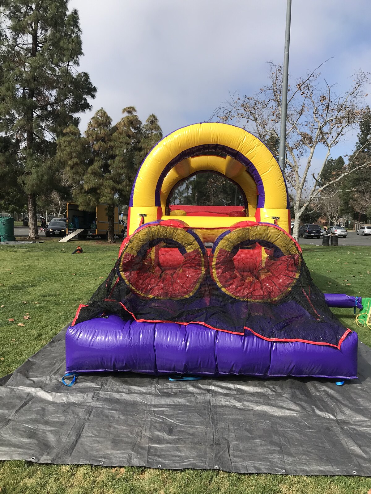 30ft backyard obstacle course rental in San Diego, front view of the purple and yellow entry arch with twin crawl-through tunnels