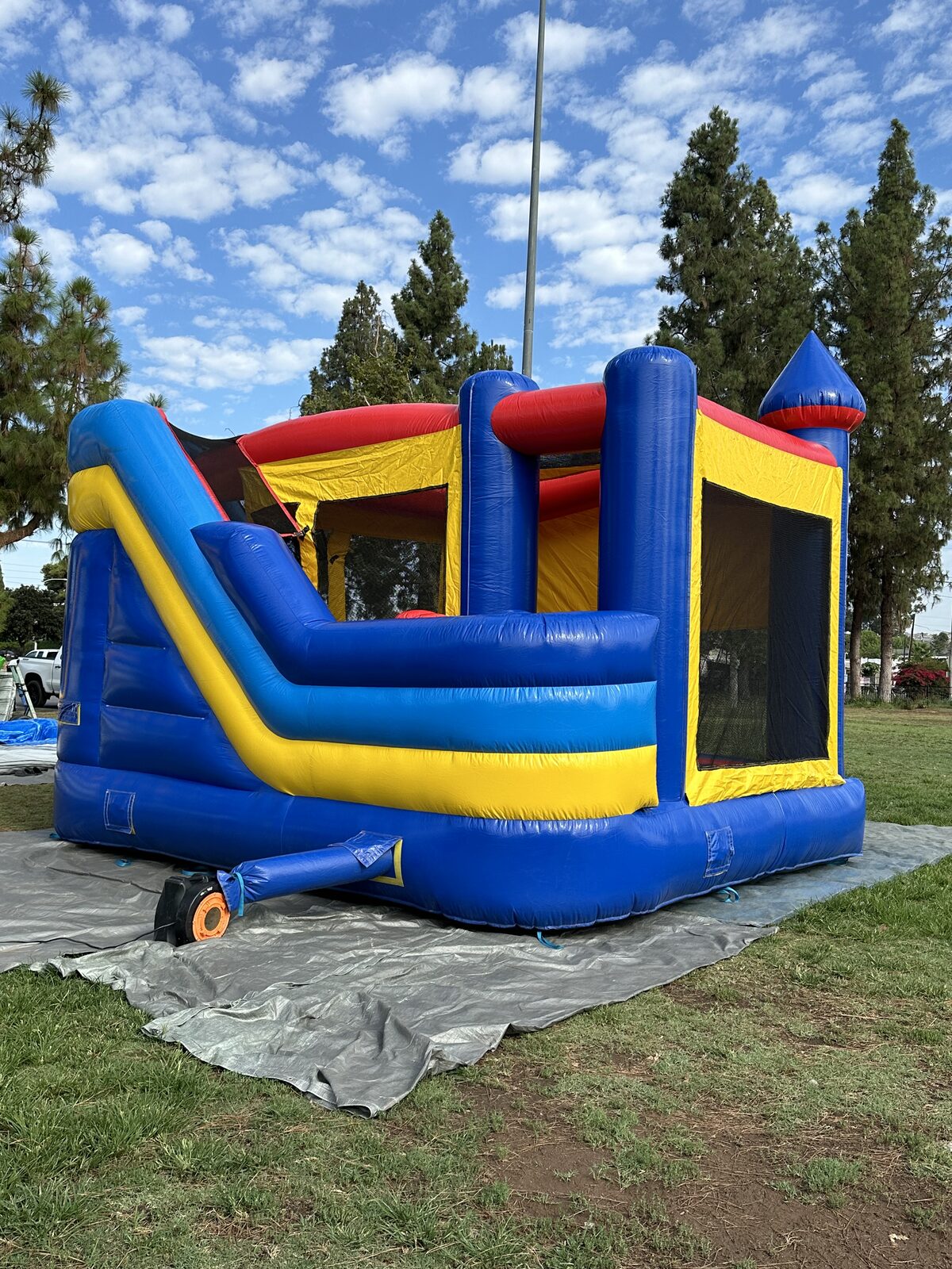 6n1 blue castle banner combo bounce house rental in San Diego, rear three-quarter view showing the slide run, blower hose and mesh side windows