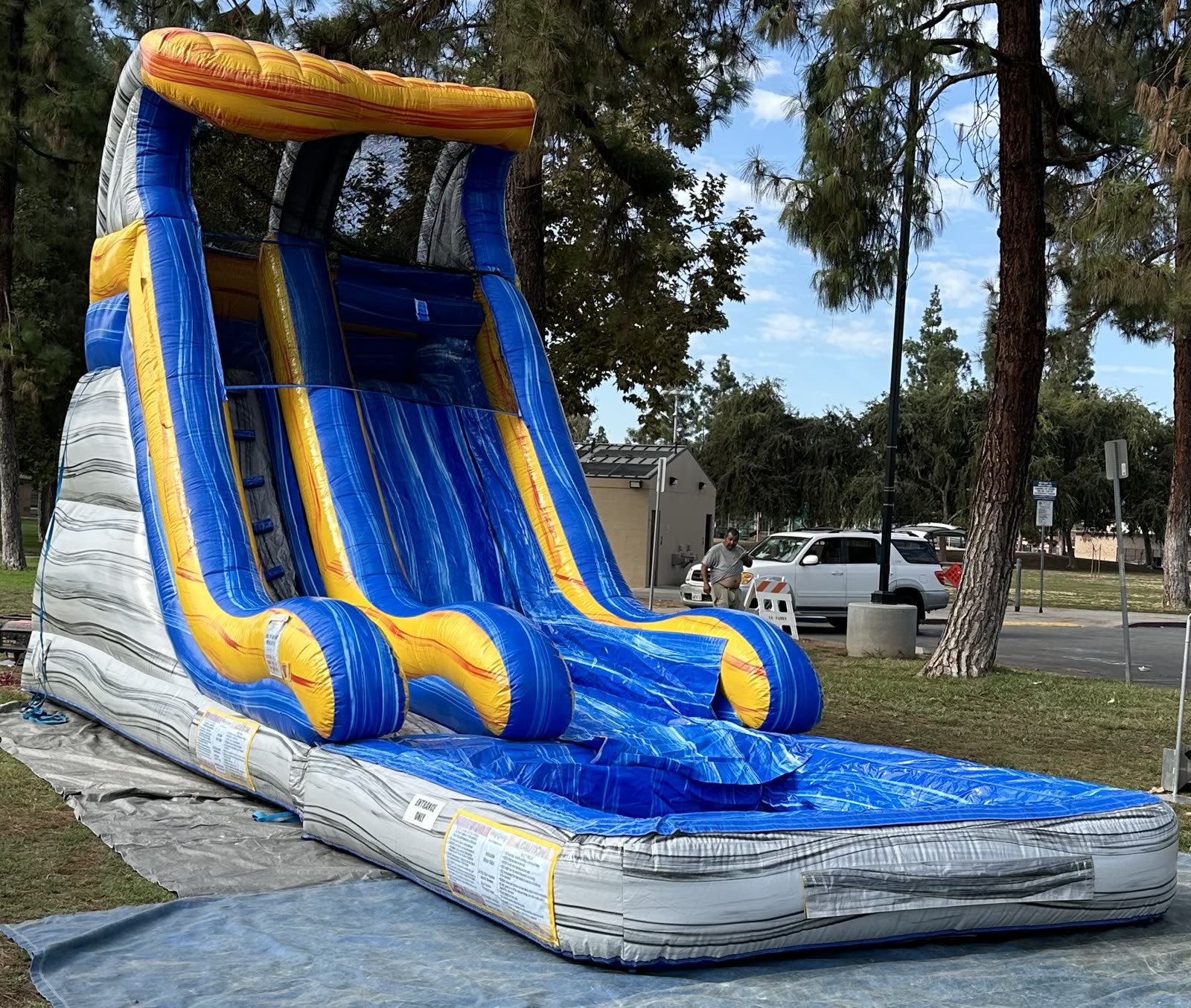 Water slide rental in San Diego, 18ft tidal wave setup wide side view at a park showing the safety instruction panels