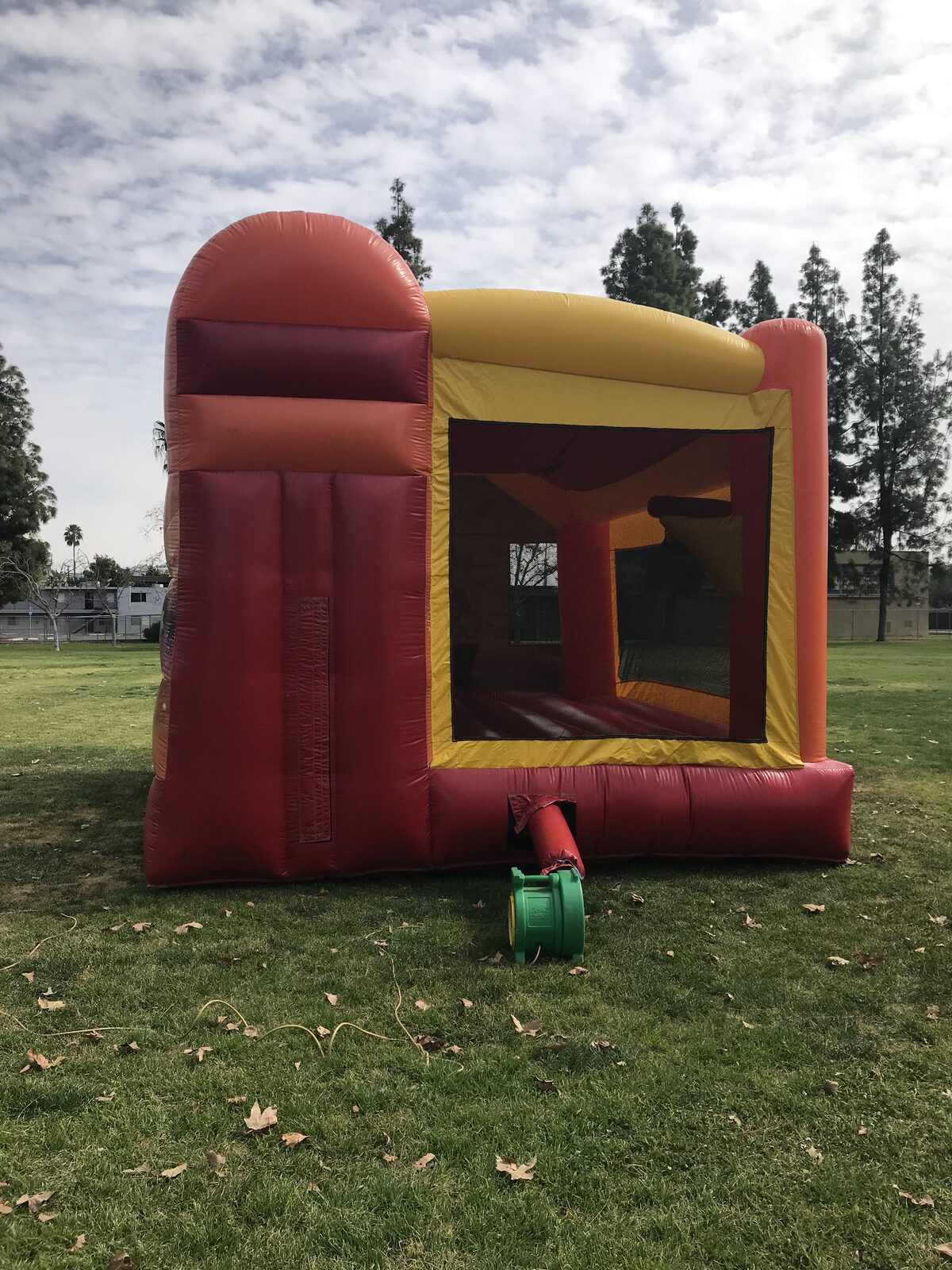 4n1 fairies combo bounce house rental in San Diego, side view of the red, orange, and yellow unit with the slide bump-out and blower hooked up on park grass