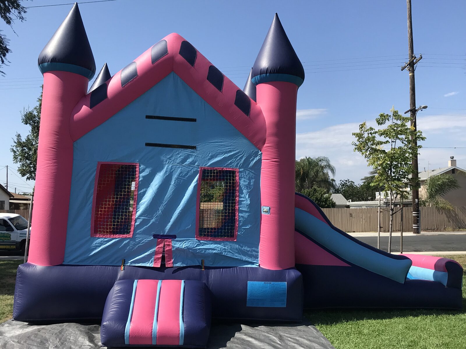 2n1 pink princess combo bounce house rental in San Diego, front view of the pink and light blue castle with navy turrets and side slide on a tarp over grass