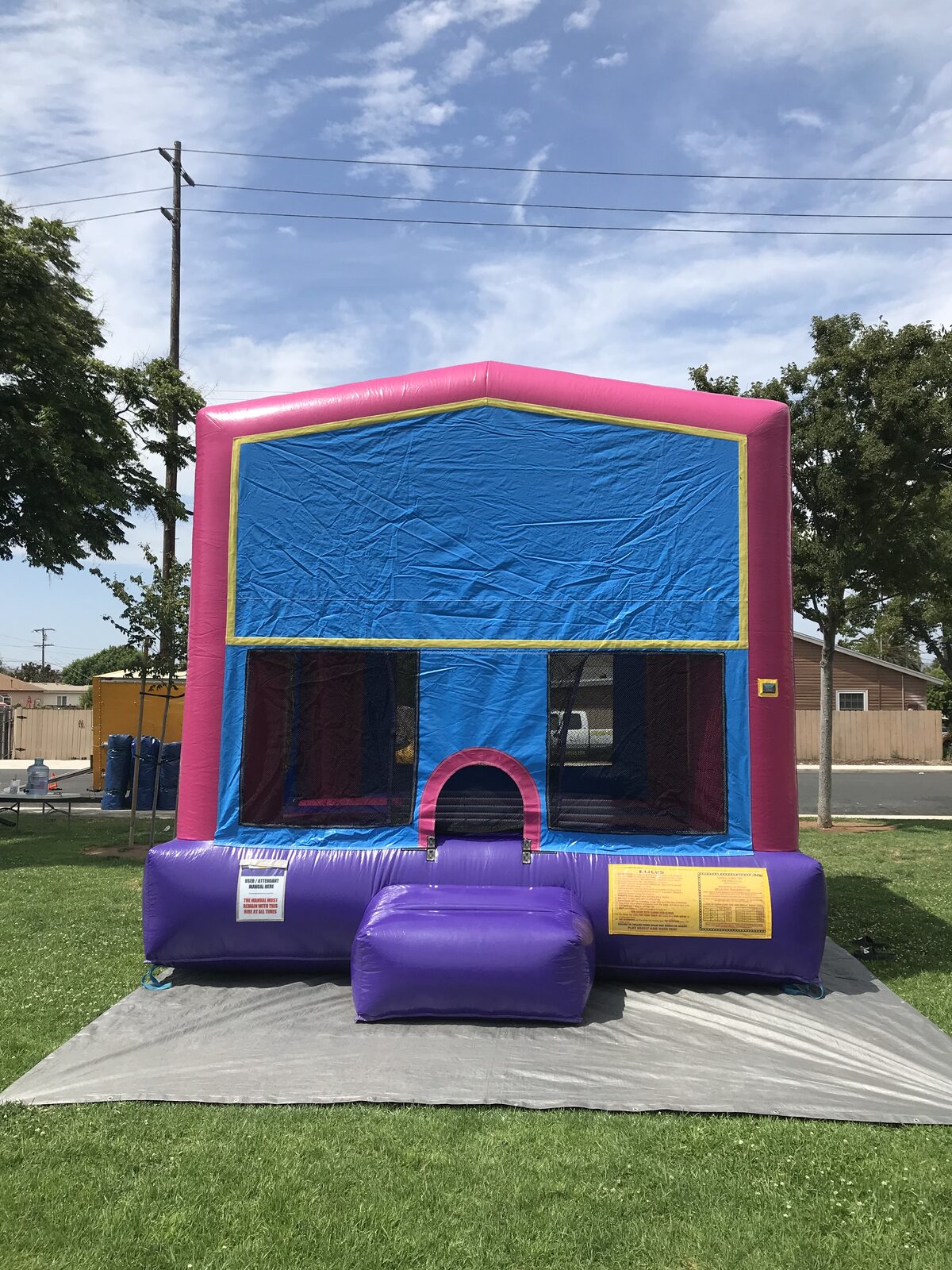 13x13 pink banner bounce house rental in San Diego — straight-on front view on a park lawn showing the pink entry arch and safety ramp